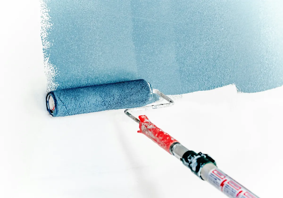 Farbroller trägt blaue Wandfarbe auf eine weiße Wand auf